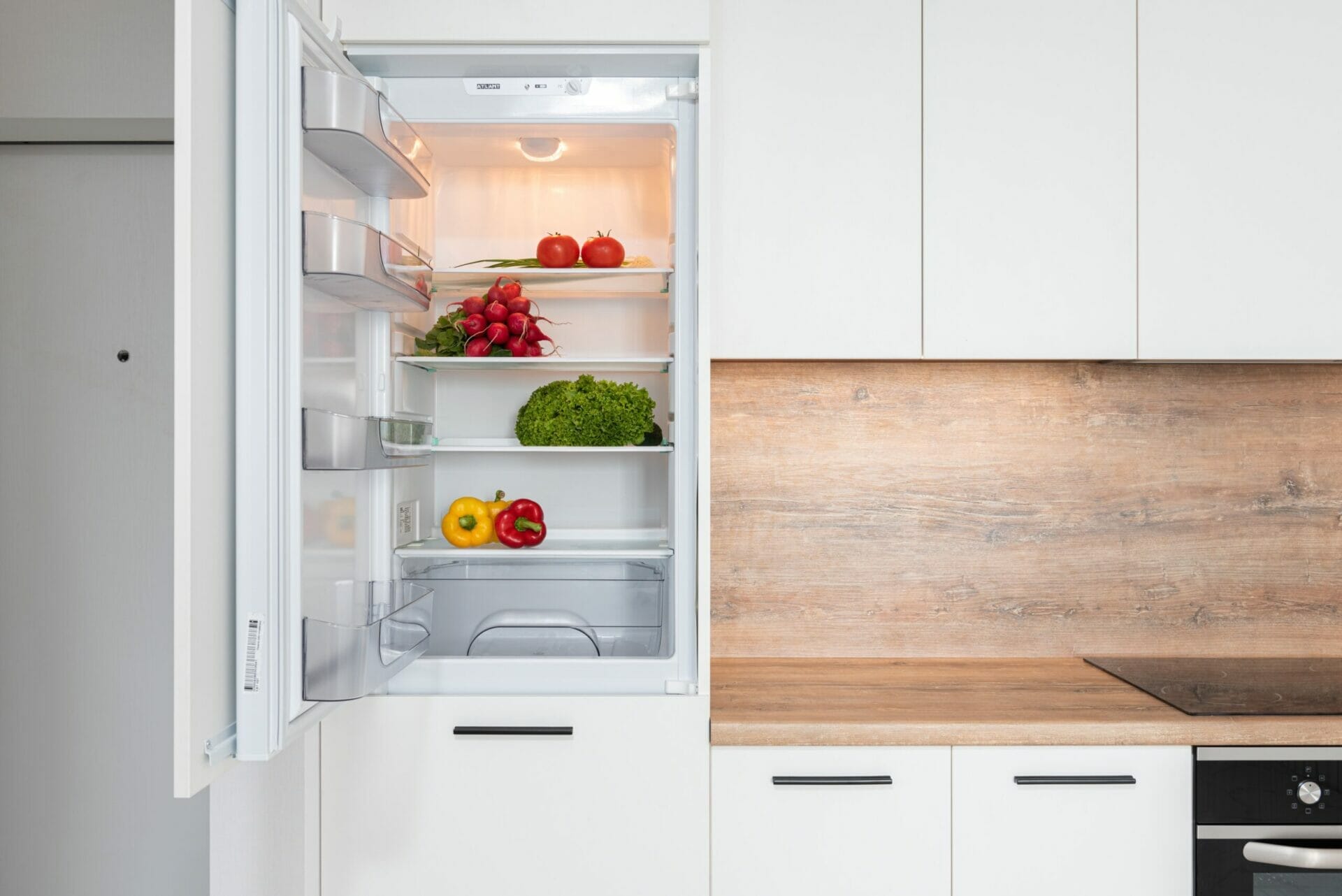 Kitchen view with fridge door open, various fresh fruit & veg inside fridge
