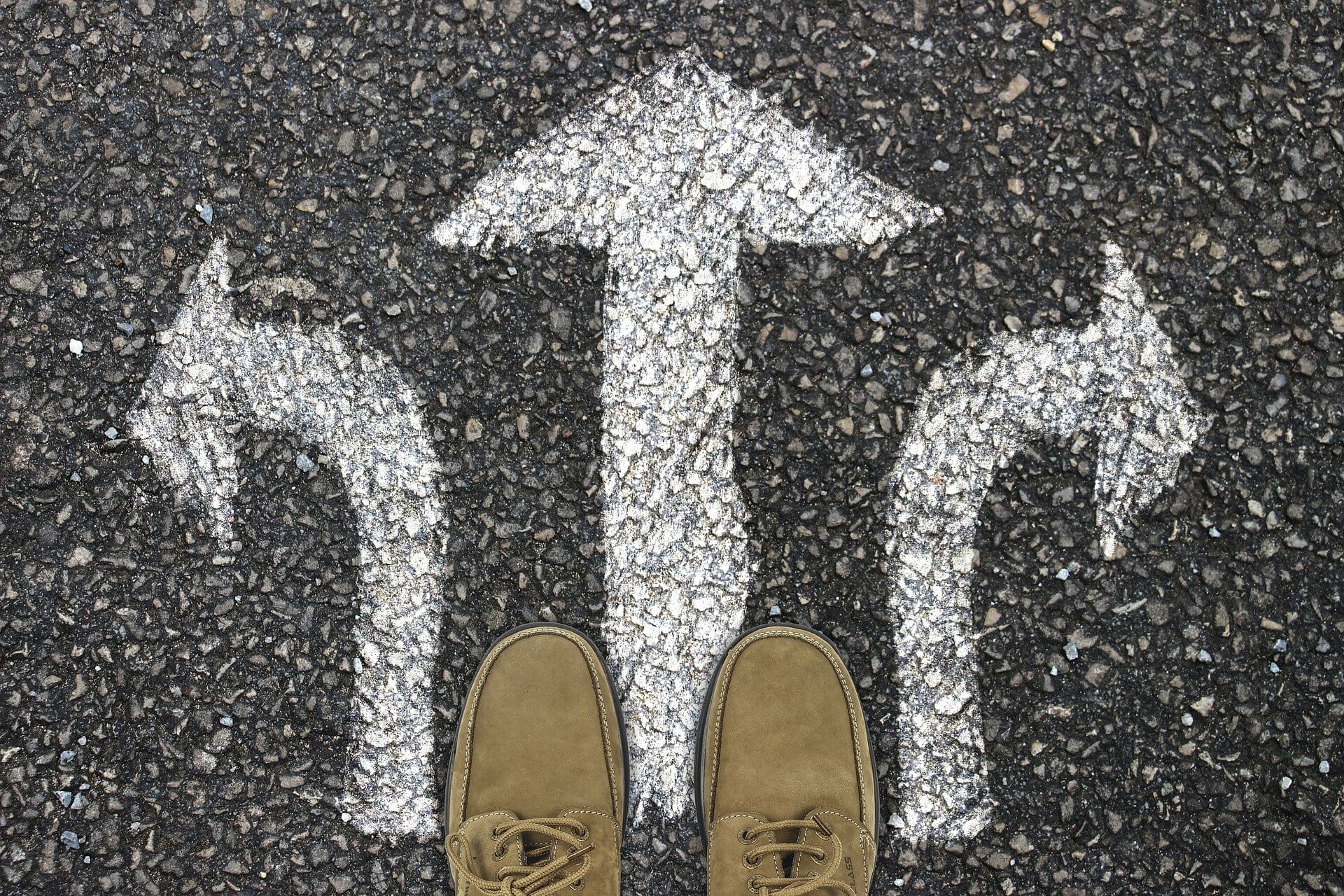 Tarmac surface man's shoes. Three painted arrows point, left, right and straight ahead.
