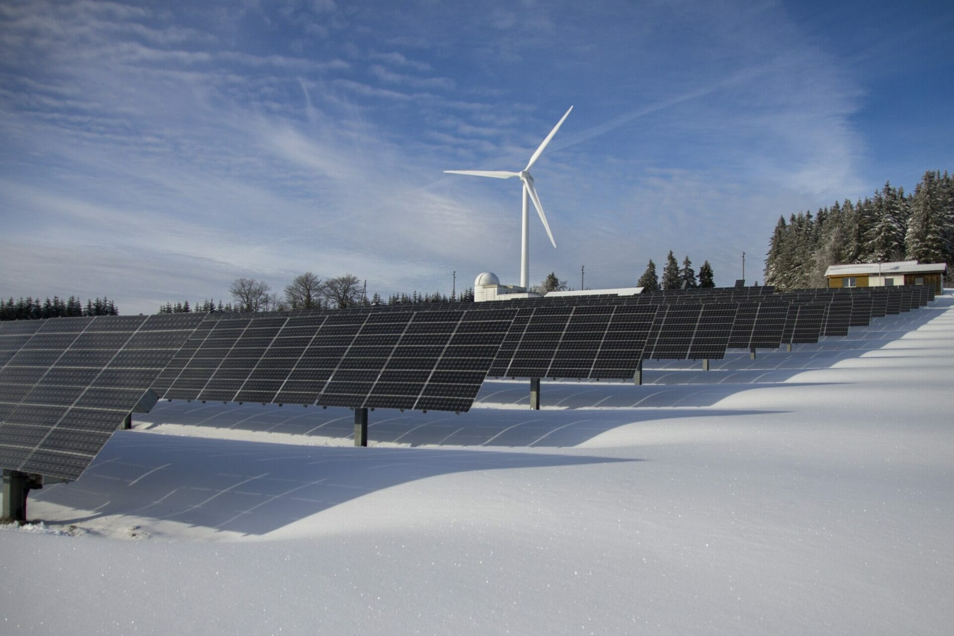 Snow covered hill, foreground solar panel farm, wind turbine in background