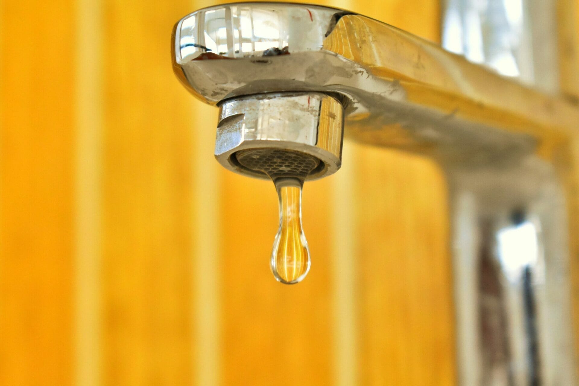 Yellow backdrop, kitchen sink tap with large drip of water