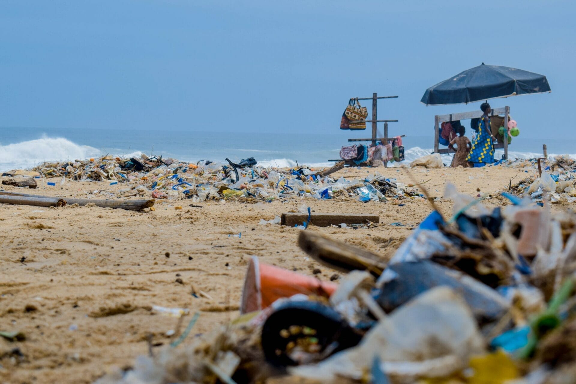Beach with sky view, parasol in background and plastic littered in foreground